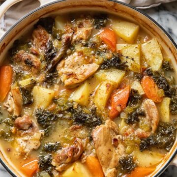Top down view of chicken stew in a large pot with carrots potatoes and herbs