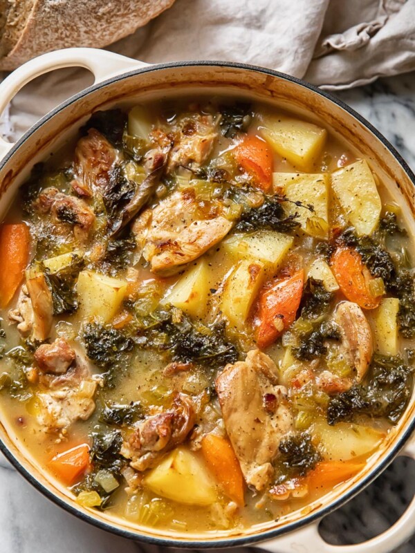 Top down view of chicken stew in a large pot with carrots potatoes and herbs