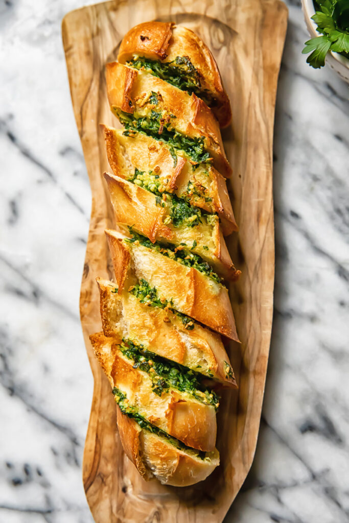 Top down shot of cheesy air fryer garlic bread on a cutting board with parsley