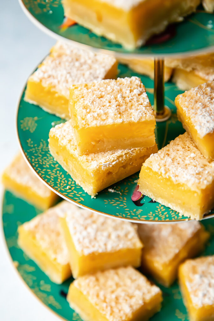 Side shot of many lemon bar pieces dusted with powder sugar on a platter