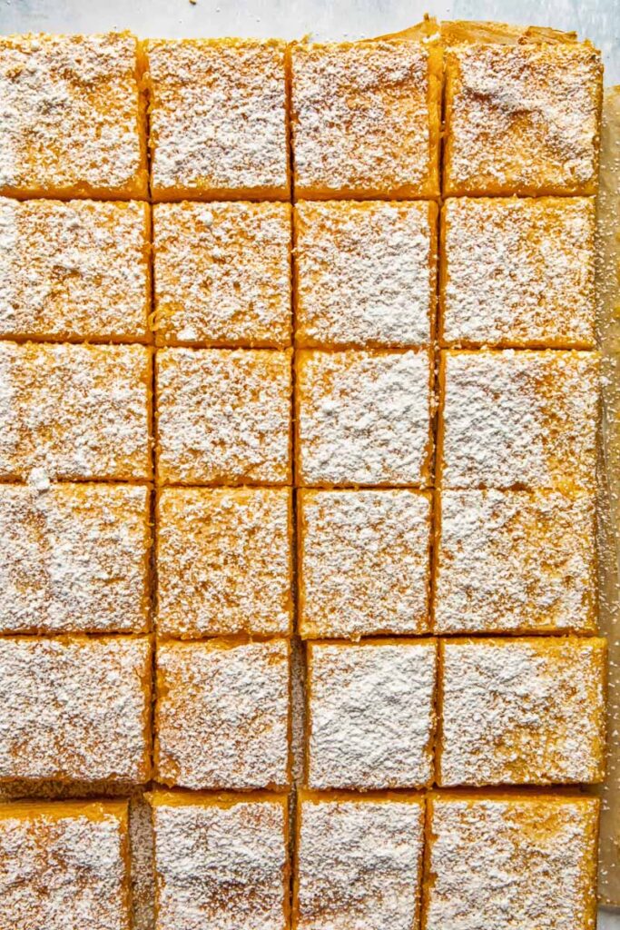 Top down shot of lemon bars being cut into pieces on a baking sheet