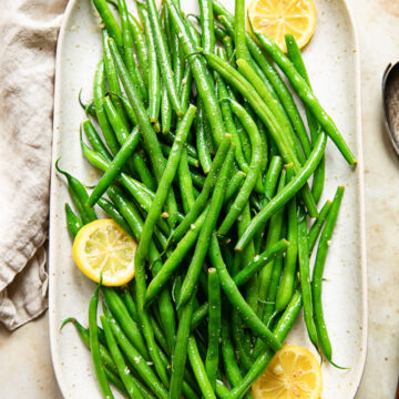 Platter of green beans with lemon butter, with visible lemon slices.