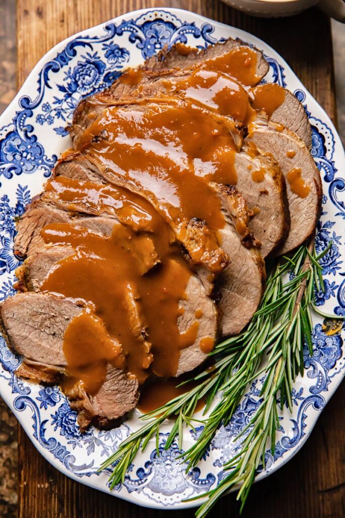 Top down shot of slow cooker roast beef on a plate with gravy and rosemary