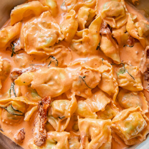pan of tortellini in cream sauce with sun-dried tomatoes with sprinkled parmesan cheese