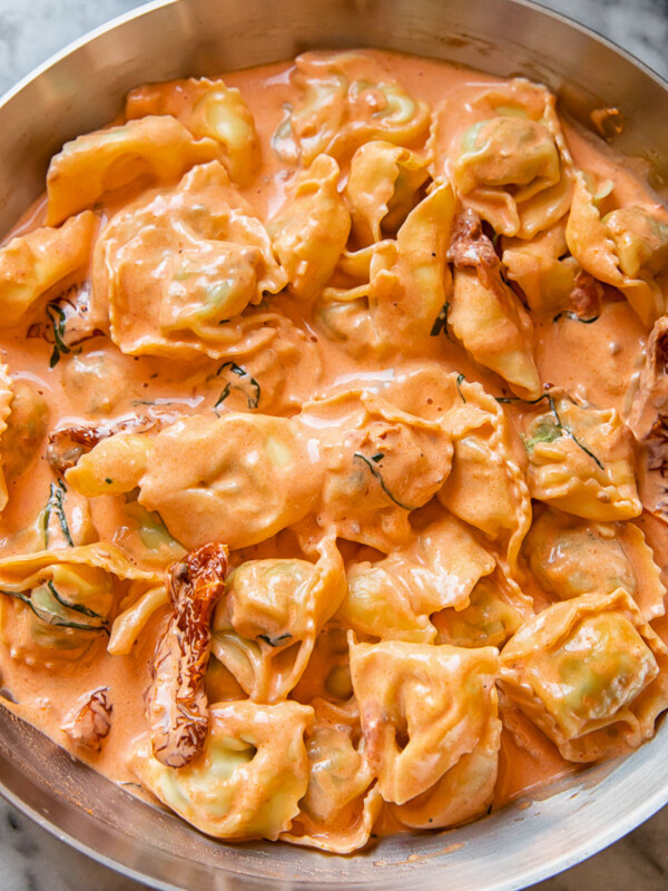 pan of tortellini in cream sauce with sun-dried tomatoes with sprinkled parmesan cheese