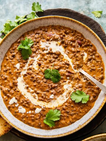 Dal makhani in a bowl with a spoon and leaves of parsley