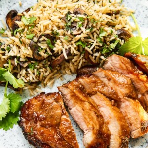 Top down view of boneless porck chop slices on a plate with herbed mushroom rice