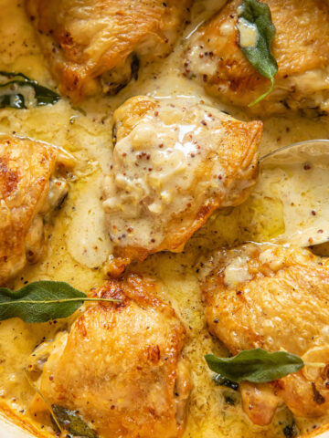 Close up view of chicken thighs braised in a creamy sage sauce in a large pan