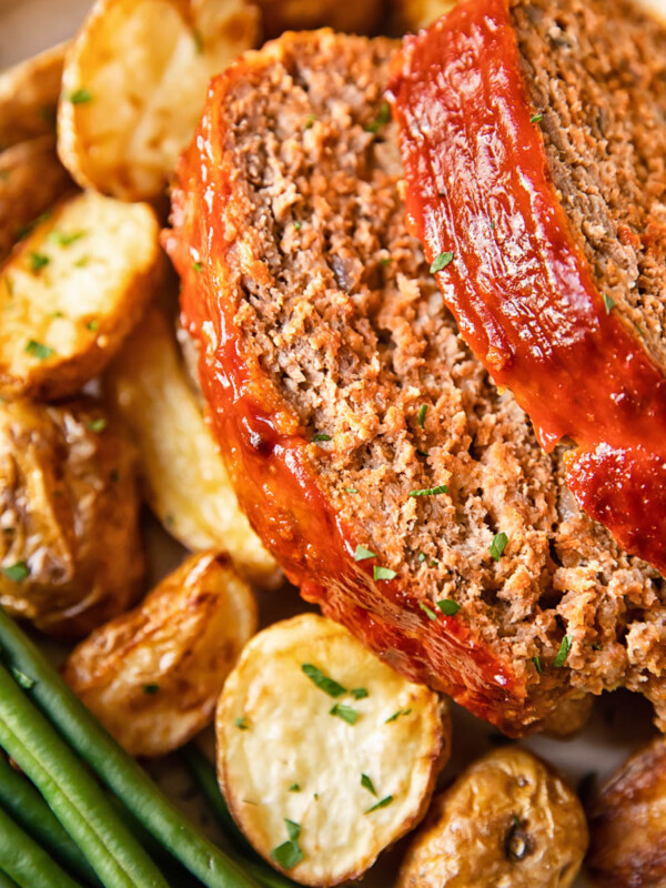 Close up shot of slices of classic meatloaf on a plate with potatoes and beans