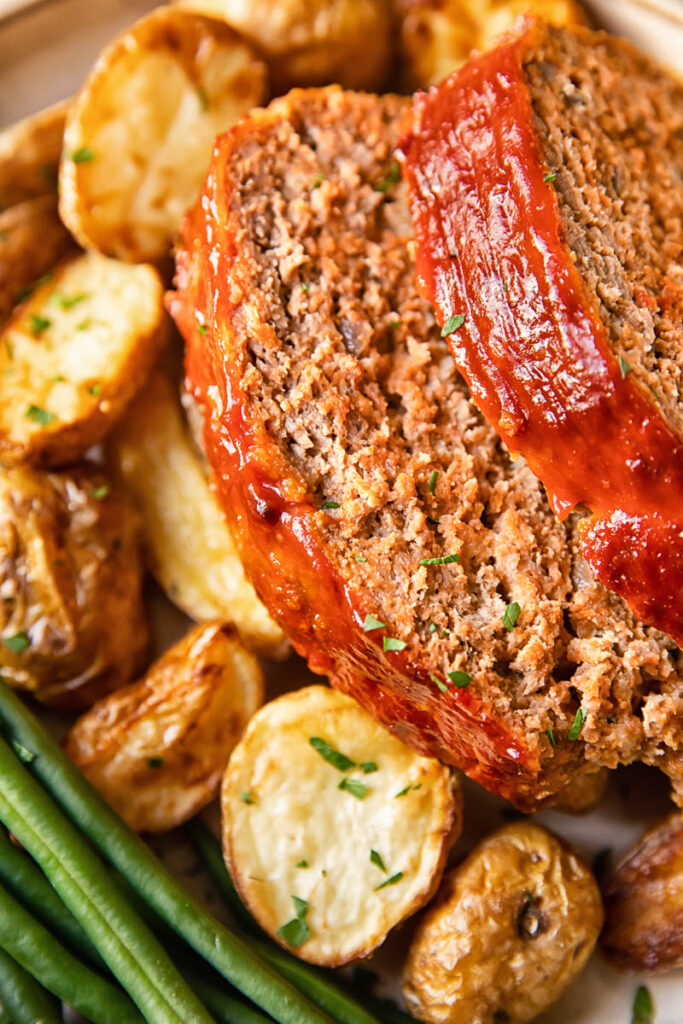 Close up shot of slices of classic meatloaf on a plate with potatoes and beans