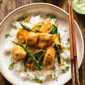 Top down shot of peanut butter chicken on top rice with beans and green onions in a bowl with chop sticks
