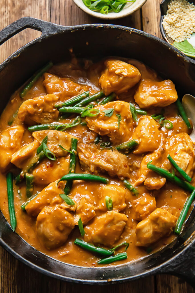 Top down shots of chicken and green beans with peanut butter sauce in a pan