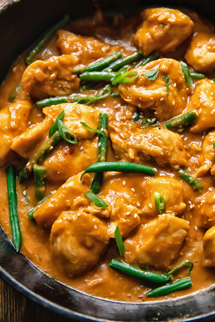 Close up shot of peanut butter chicken in a ban with green beans and green onions