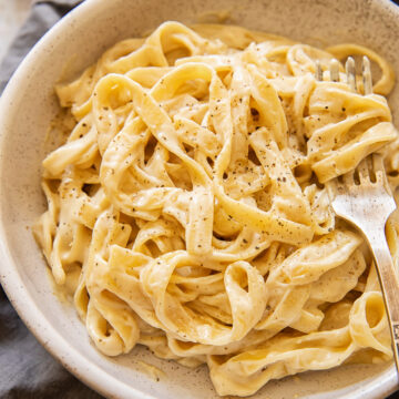Bowl of vegan Alfredo sauce with sprinkling of pepper and a fork