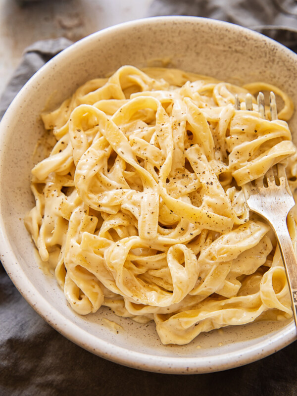 Bowl of vegan Alfredo sauce with sprinkling of pepper and a fork