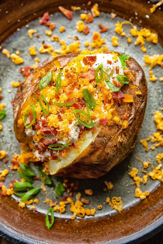 Top down shot of a baked potato, sliced open and topped with sour cream, bacon, cheese and green onions