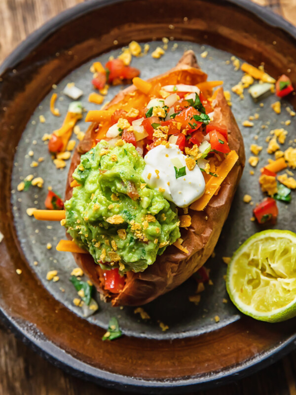 Top down shot of baked sweet potato on a plate topped with pico de gallo and guacamole