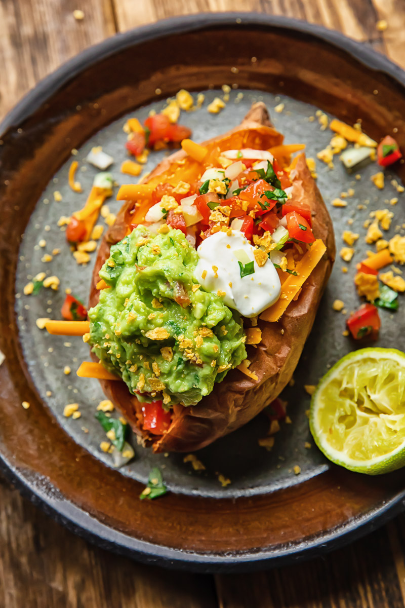 Top down shot of baked sweet potato on a plate topped with pico de gallo and guacamole