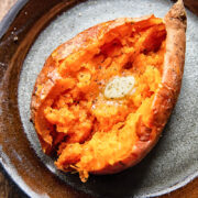 Close up shot of a cut open baked sweet potato topped with melted butter on a plate