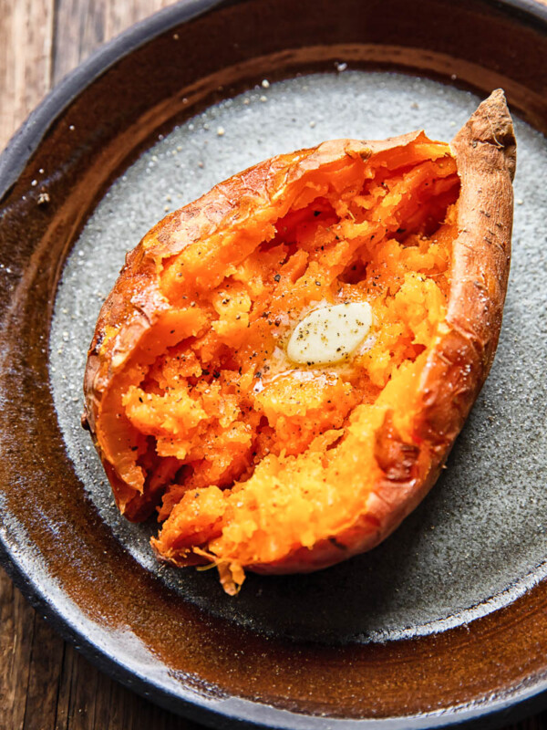 Close up shot of a cut open baked sweet potato topped with melted butter on a plate