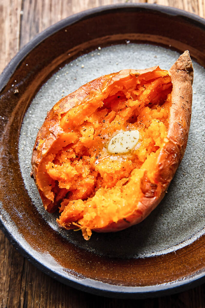 Close up shot of a cut open baked sweet potato topped with melted butter on a plate