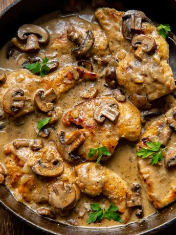 chicken cutlets and mushrooms in a sauce, topped with parsley garnish in a cast iron pan