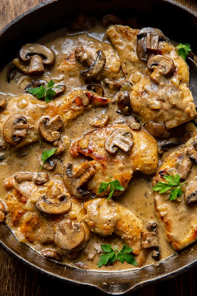 chicken cutlets and mushrooms in a sauce, topped with parsley garnish in a cast iron pan