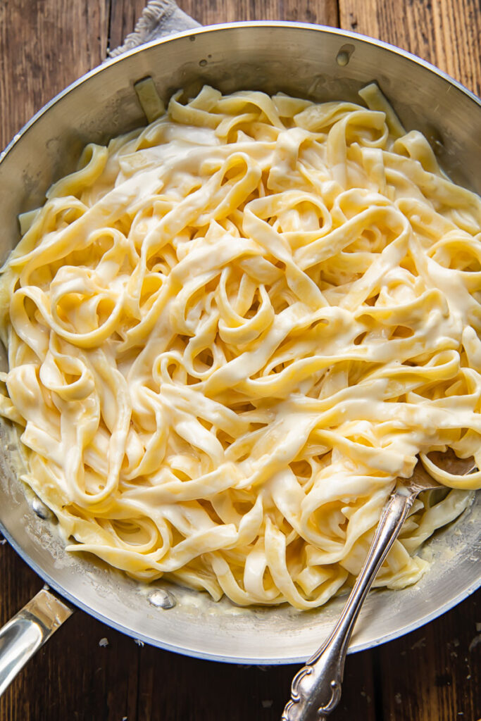 Top down shot of fettucine pasta in a pan with creamy alfredo sauce