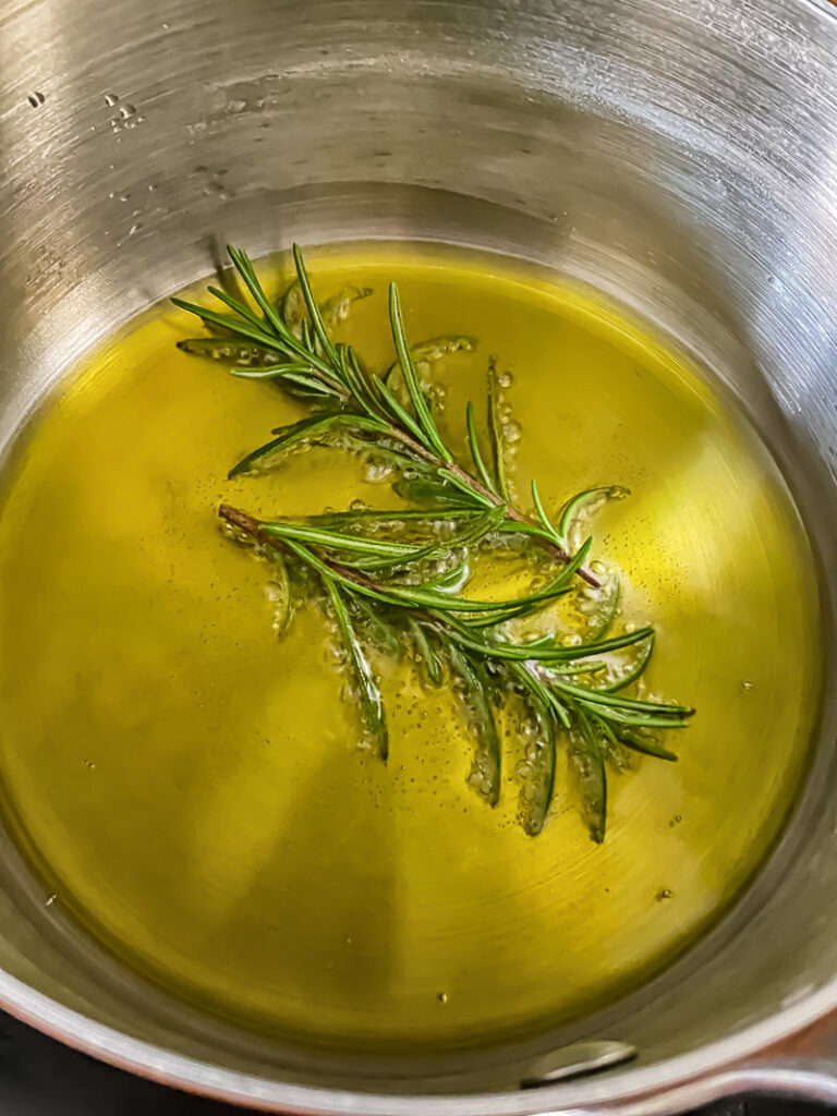 Inside of a saucepan showing olive oil and rosemary