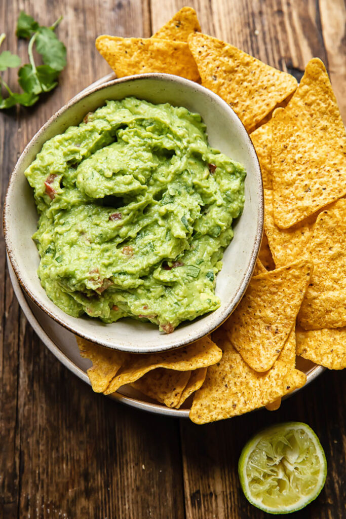 bowl of guacamole on plate with tortilla chips
