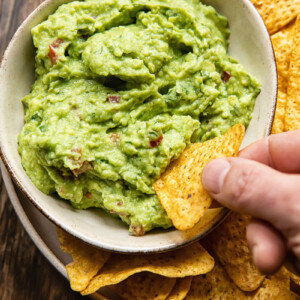 bowl of guacamole with hand dipping tortilla chip in