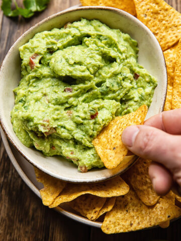 bowl of guacamole with hand dipping tortilla chip in