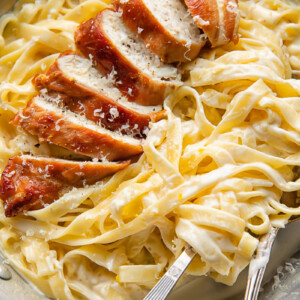 Top down shot of prosciutto wrapped chicken alfredo with creamy fettucine in a bowl with a fork