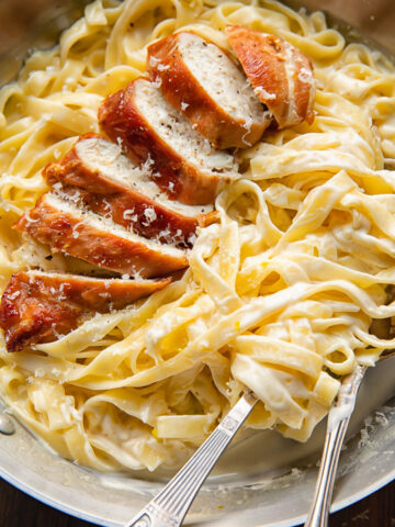 Top down shot of prosciutto wrapped chicken alfredo with creamy fettucine in a bowl with a fork