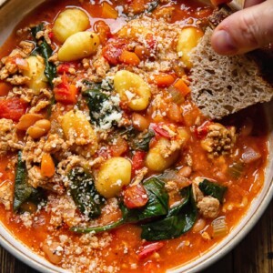 bowl of sausage gnocchi soup with hand dipping piece of bread