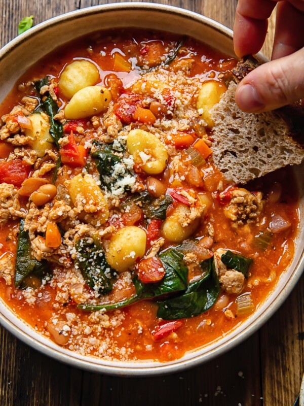 bowl of sausage gnocchi soup with hand dipping piece of bread