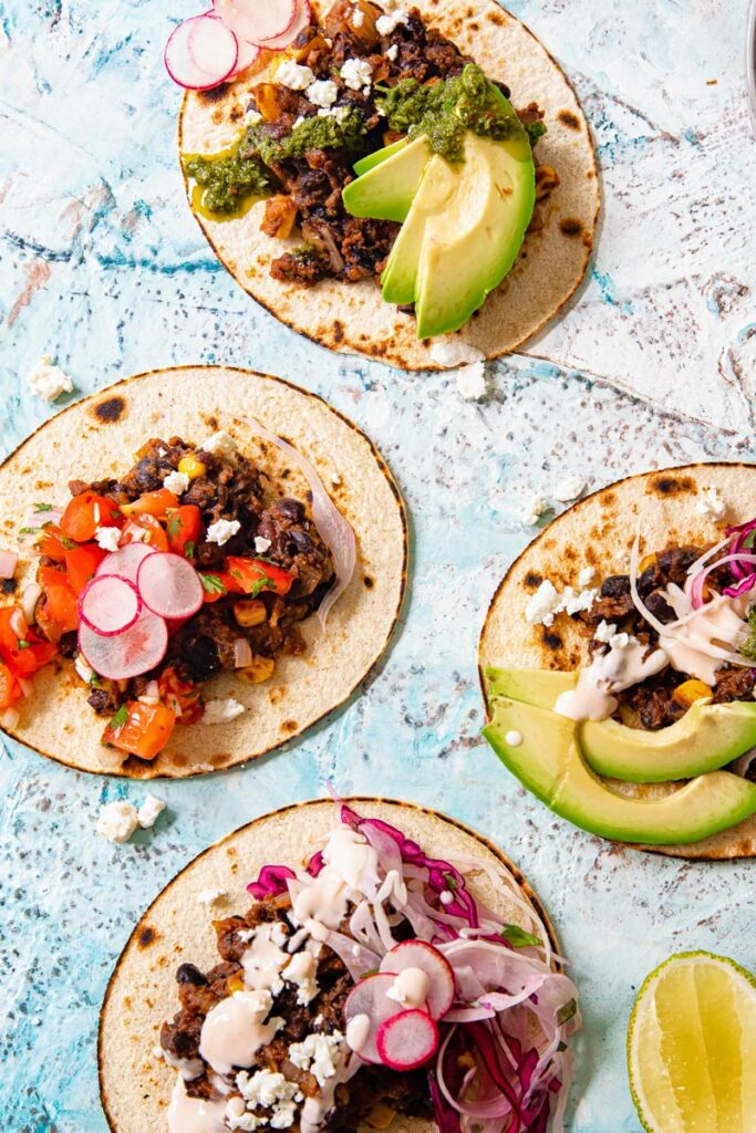 Four black bean and corn tacos lying open with range of toppings