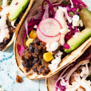 Close up of a black bean and corn taco showing radish and cilantro lime slaw and slice of avocado