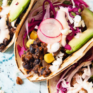 Close up of a black bean and corn taco showing radish and cilantro lime slaw and slice of avocado