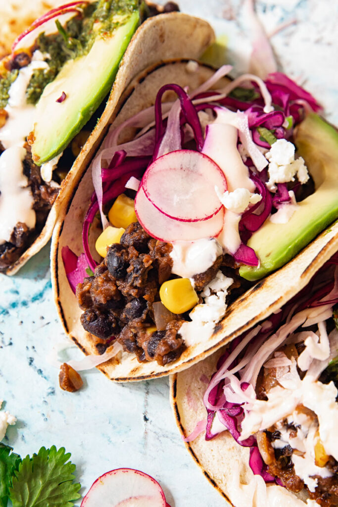 Close up of a black bean and corn taco showing radish and cilantro lime slaw and slice of avocado