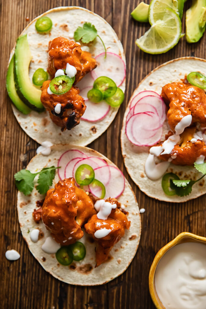 Buffalo cauliflower tacos with toppings on a tabletop