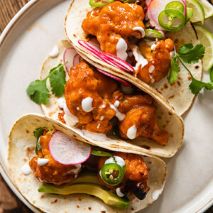 Buffalo cauliflower tacos folded and leaning together on a plate