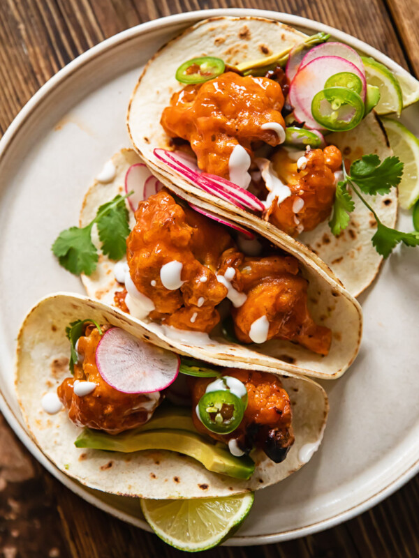 Buffalo cauliflower tacos folded and leaning together on a plate