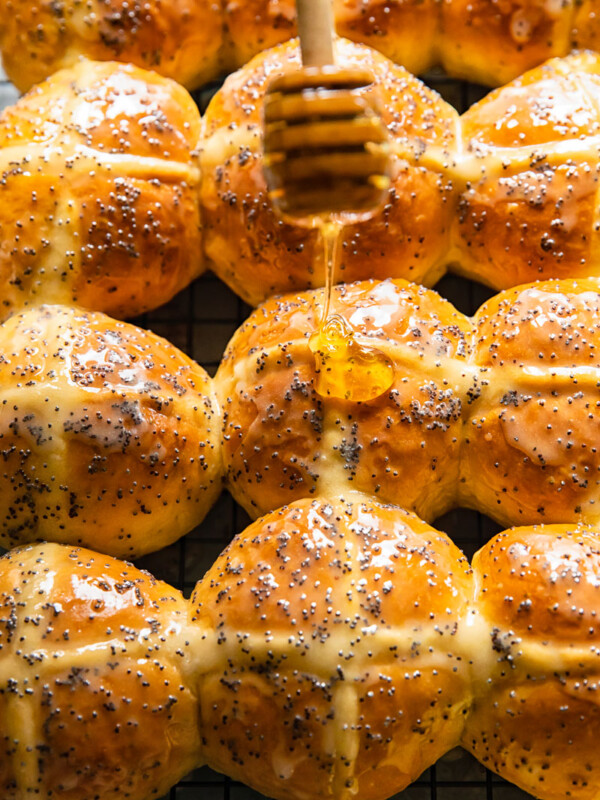 honey being drizzled on top of a hot cross bun