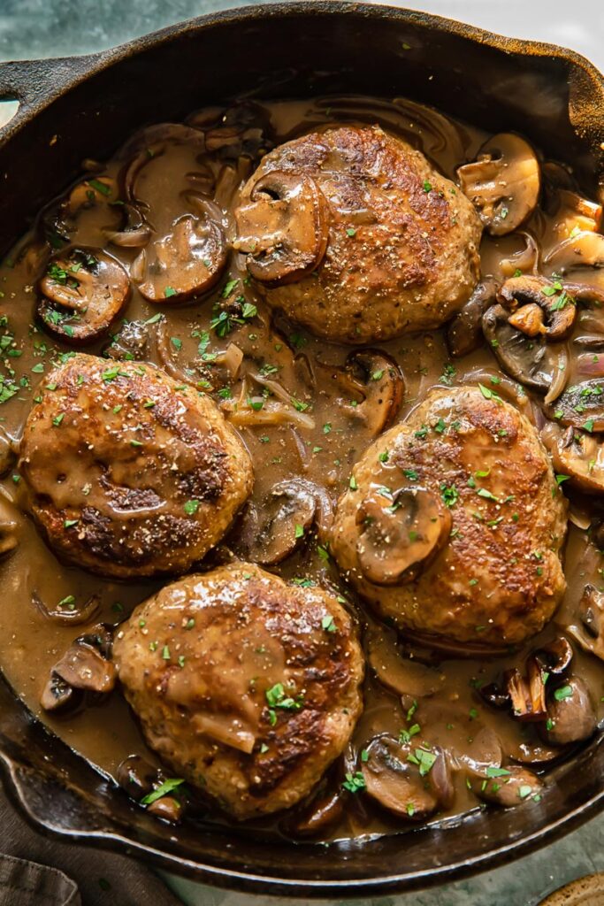 Top down shot oh a cast iron pan with salisbury steaks in an onion mushroom gravy