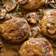 Close up shot of salisbury steaks in a pan with mushrooms in a creamy sauce