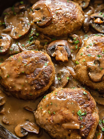 Close up shot of salisbury steaks in a pan with mushrooms in a creamy sauce