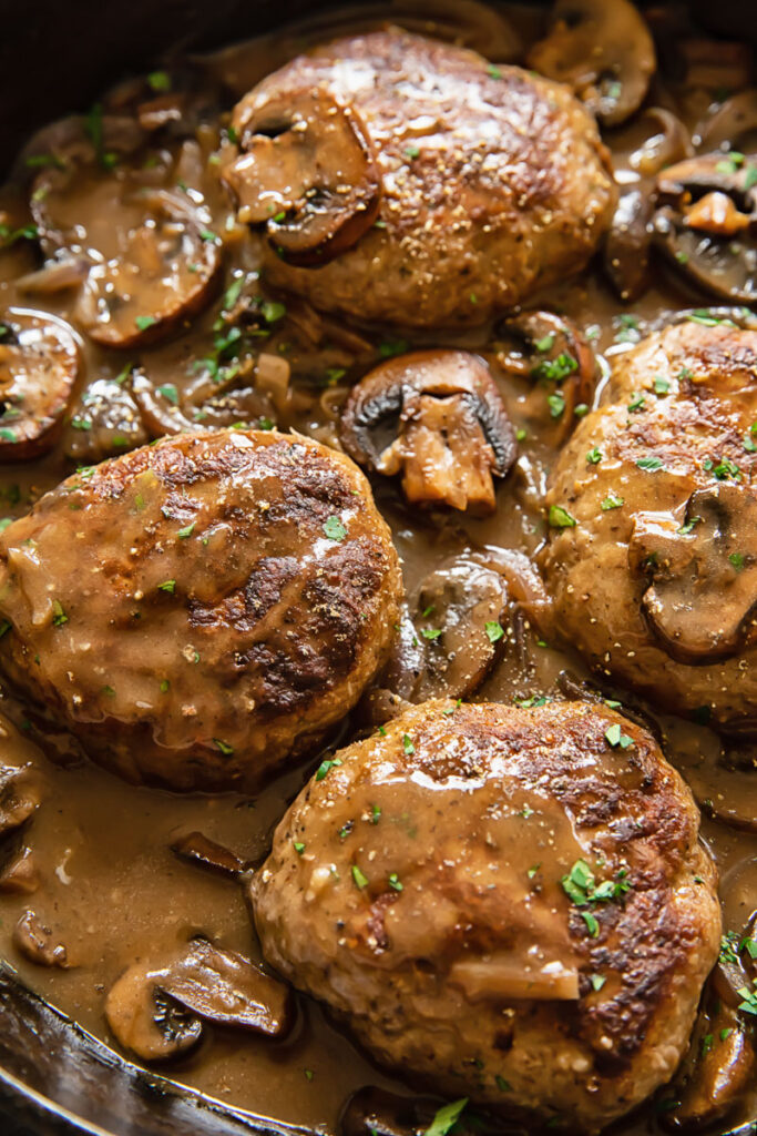 Close up shot of salisbury steaks in a pan with mushrooms in a creamy sauce