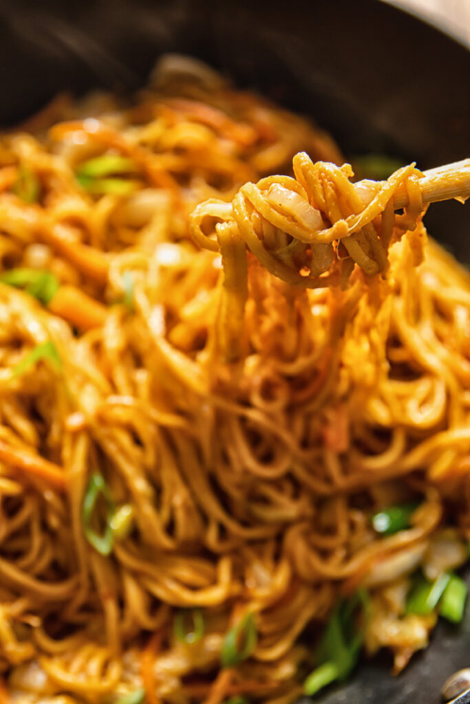 chopsticks pulling out peanut noodles from a wok