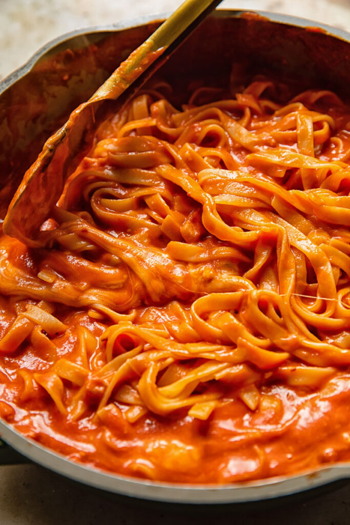 pan with tagliatelle in a red sauce stirred by tongs
